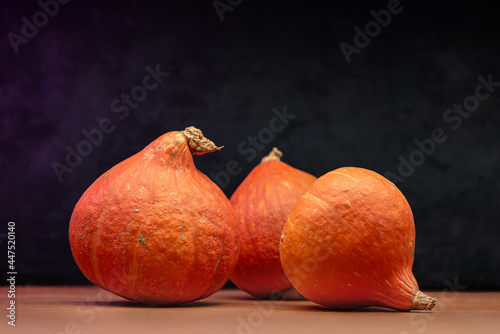 Three Ripe Beautiful Pumpkins Have Been Placed On A Wooden Table. Black Textured Background In The Background.