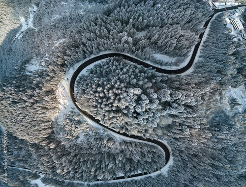 Aerial view of winter landscape with snow covered mountain hills and winding forest road in morning. © bilanol