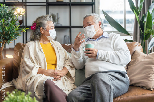 happiness asian senior couple sit relax morning conversation on sofa in living room,old asian people wearing mask siting on sofa at home home isolation ideas concept