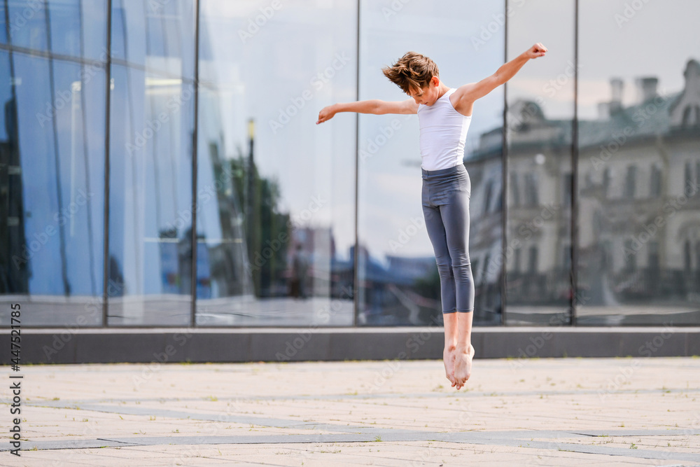 ballet boy teenager dancing in a jump against background of city and sky reflections in a glass wall