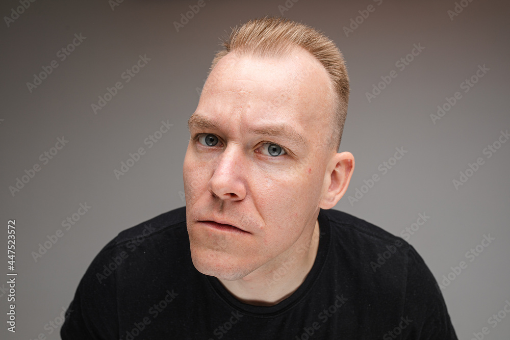 portrait of beautiful caucasian male in black t-shirt looks at camera and tries to see something, picture isolated on grey background