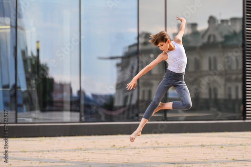 Fototapeta Naklejka Na Ścianę i Meble -  ballet boy teenager dancing against the background of reflection of the city and sky in the glass wall