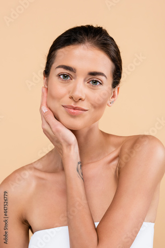 sensual woman with naked shoulders touching face while posing isolated on beige, beauty concept