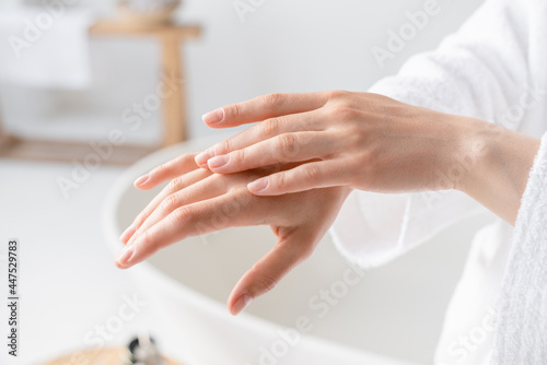 Cropped close up photo of young woman`s hands applying moisturizer cream body oil for smooth effect in spa. Home body care. Beauty recreation treatment