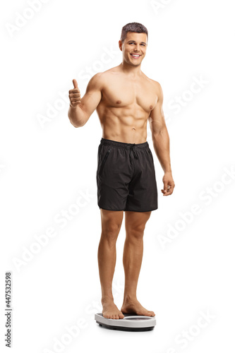 Full length shot of a shirtless muscular man standing on a weight scale and showing thumbs up photo