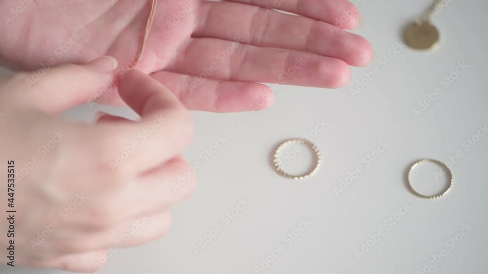 Young woman hands take gold necklace with white precious stone from among rings and jewelry on white table extreme closeup Young woman hands take gold necklace with white precious stone from among rings and jewelry on white table extreme closeup