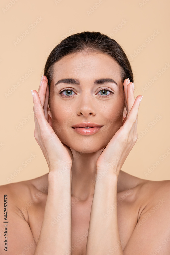 front view of brunette woman with hands near perfect face isolated on beige, beauty concept