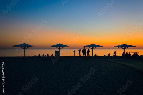 A beach with beach umbrellas and people on a summer evening at sunset