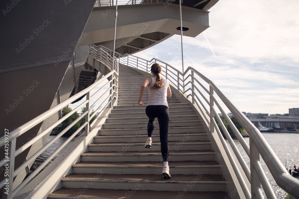 An athlete girl runs up the stairs of the bridge. Evening strength running workout in the city. Preparing for the competition.