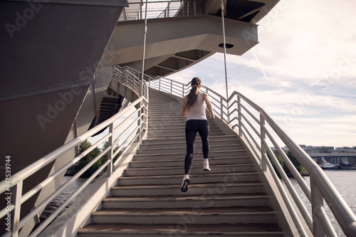 A young woman runs up the stairs of the bridge. Power training. Running in the evening in the city