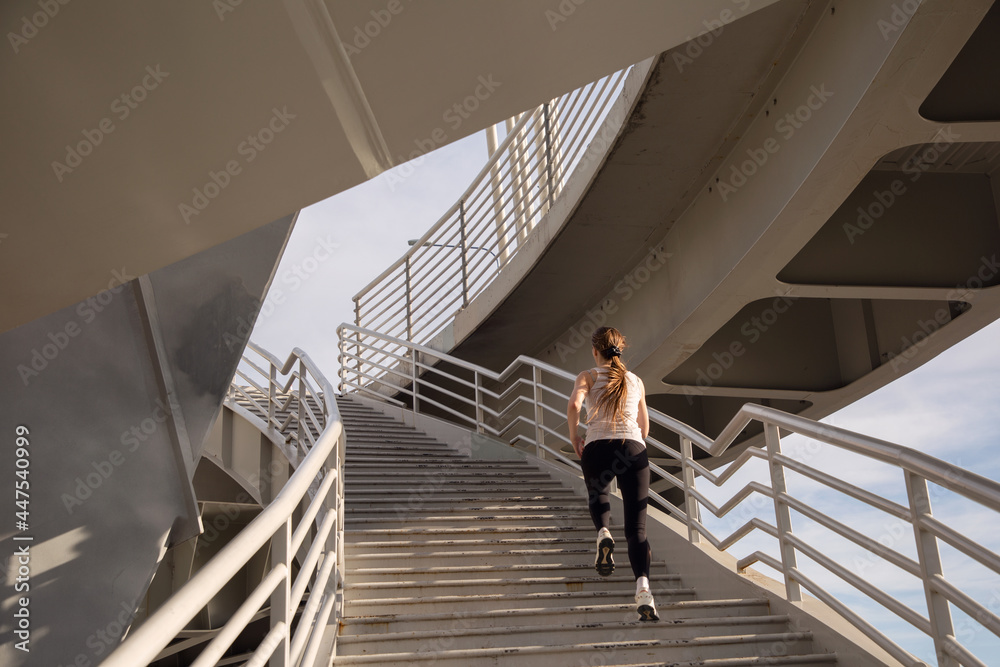 A sportswoman runs along the steps of the stairs of the bridge. Power training.