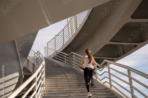An athlete girl runs up the stairs of the bridge. Evening strength running workout in the city. Preparing for the competition.