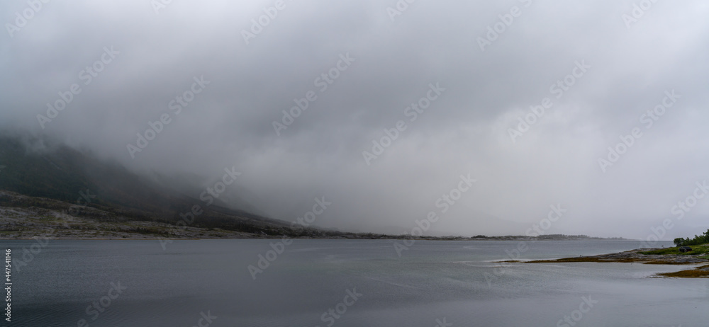 panorama landscape view of a fjord with mystical fog and cloud cover coming down from the mountains over the ocean panorama landscape view of a fjord with mystical fog and cloud cover coming down from the mountains over the ocean