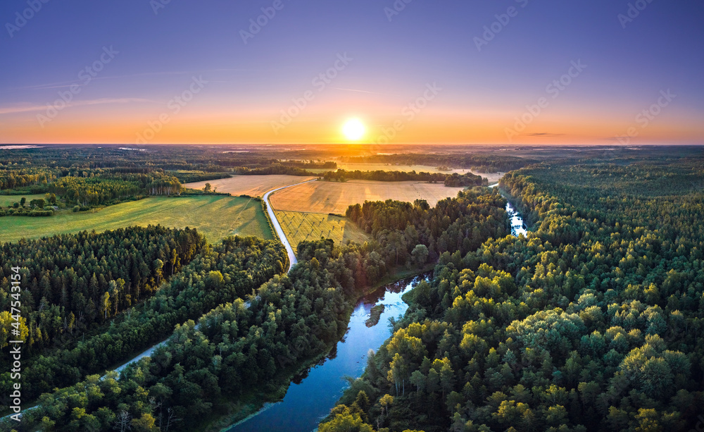 Aerial view over countryside at warm sunrise tones. Agriculture land mixing with forest and meadows. Crop fields along the curved river. 
