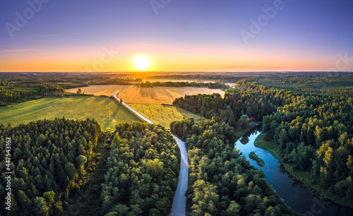 Aerial view over countryside at warm sunrise tones. Agriculture land mixing with forest and meadows. Crop fields along the curved river. 