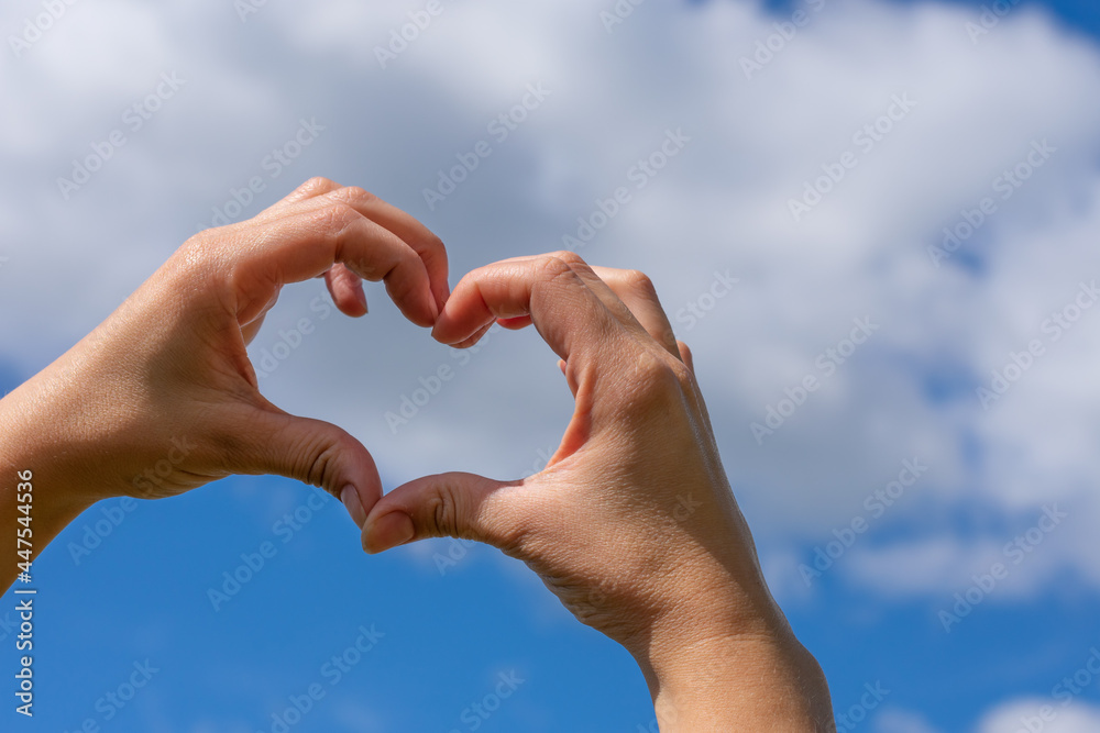 Young woman hands in heart shaped gesture on bright blue sky natural background. Copy space. Metaphor or concept of love mood, tranquility and family relationship. Bright summer sunlight Young woman hands in heart shaped gesture on bright blue sky natural background. Copy space. Metaphor or concept of love mood, tranquility and family relationship. Bright summer sunlight