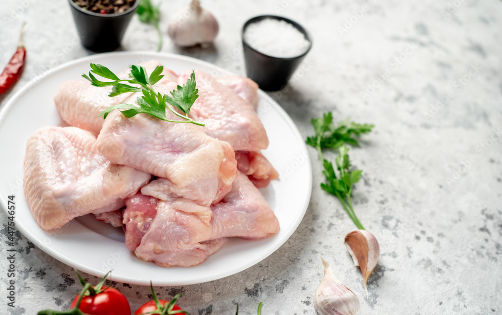 raw chicken wings on a white plate on a white stone background with copy space for your text