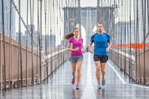 New York city runners athletes training for run marathon on Brooklyn Bridge. Fit active interracial couple on outdoor running exercise in raining day. Summer rain. Asian woman, Caucasian man.