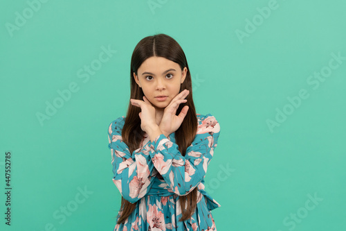 Beauty look of serious teenage girl holding hands near face blue background, skin care