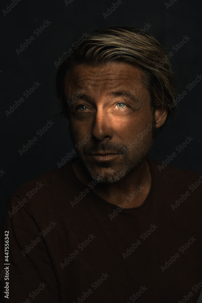 Dark mysterious portrait of a blond man with light blue eyes and