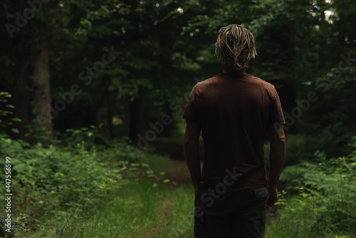 Blonde man in brown t-shirt on a forest path in summer. Rear vie
