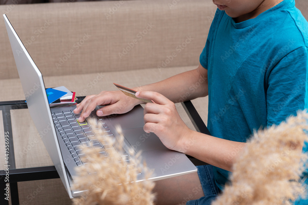 Close up image of boy's hands with credit card near laptop executing online payment. New reality, convenience on online shopping from home Close up image of boy's hands with credit card near laptop executing online payment. New reality, convenience on online shopping from home