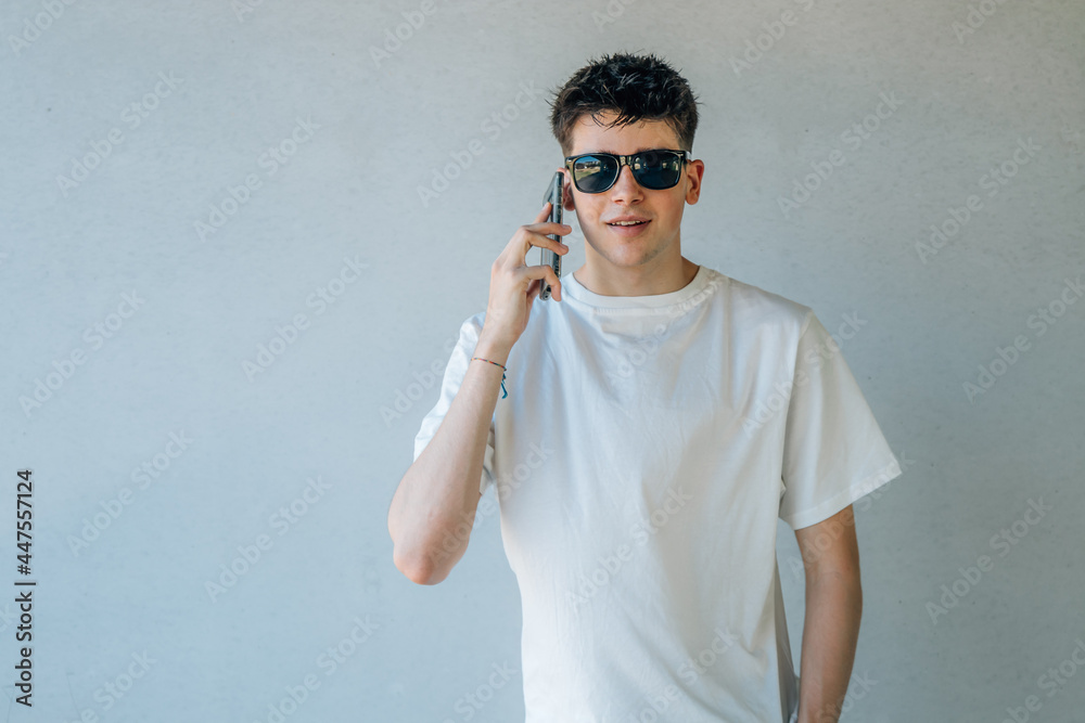 Naklejka premium teen boy with mobile phone and sunglasses isolated on wall background