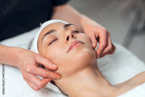 Cosmetologist making face massage for rejuvenation to woman while lying on a stretcher in the spa center. photo