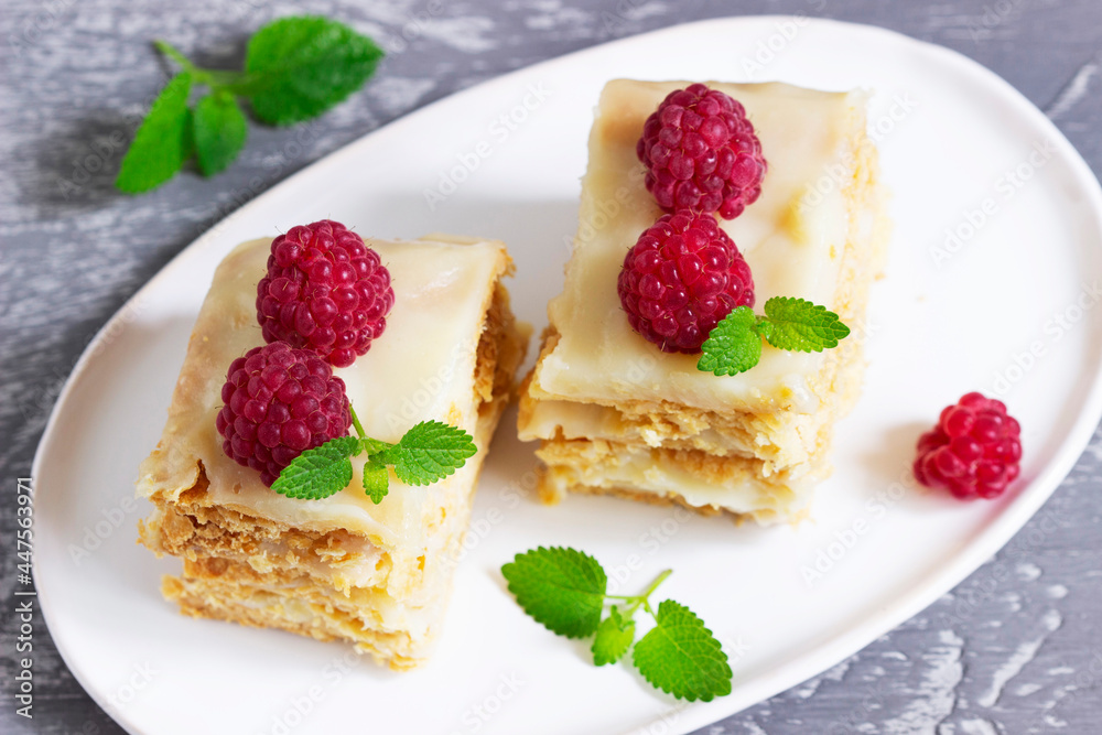 Pieces of Napoleon cake decorated with raspberries and lemon balm leaves on a light background. Pieces of Napoleon cake decorated with raspberries and lemon balm leaves on a light background.