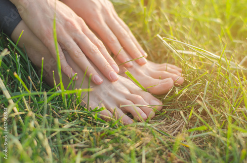 Barefoot female feet on the green lawn grass close-up. Unity with nature. Female hands lie on the legs © Анастасія Шатирова