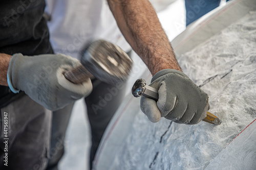 Detail of artist's hands sculpting marble with hammer and chisel