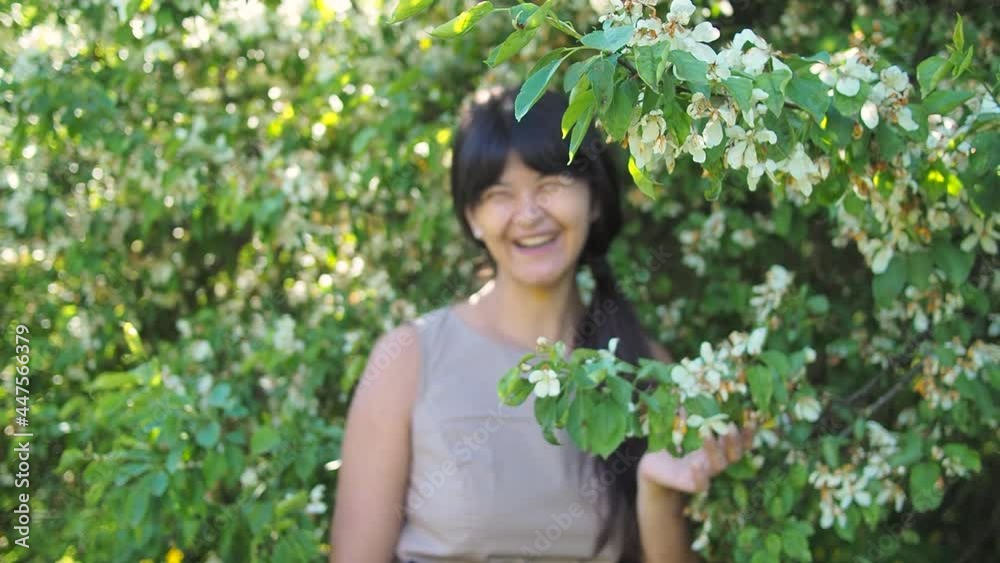 Woman portrait smiling in blossoming branch of a tree with selective focus. Young beautiful woman enjoys scent of flowers at garden Woman portrait smiling in blossoming branch of a tree with selective focus. Young beautiful woman enjoys scent of flowers at garden