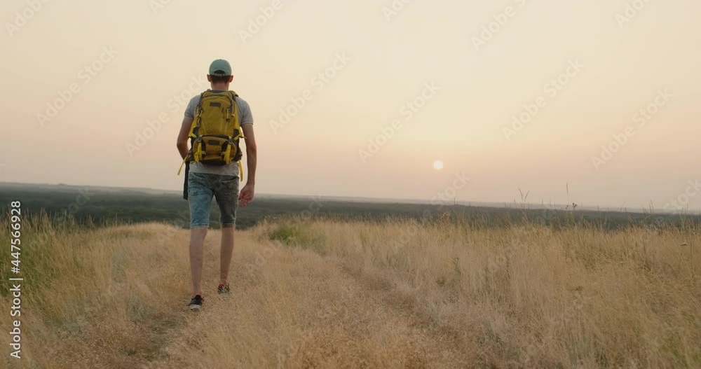 Rear View of Walking Person on Field Road. 20s Tourist Walks on an Adventure Trip Rear View of Walking Person on Field Road. 20s Tourist Walks on an Adventure Trip