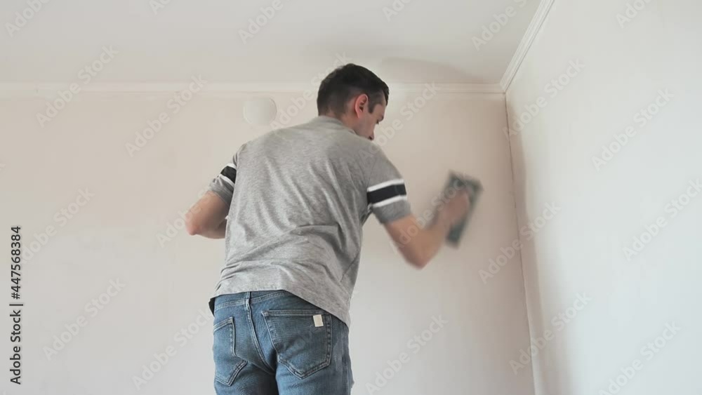 man smooth out hard putty on a wall an emery paper. Professional repair male makes renovation in apartment man smooth out hard putty on a wall an emery paper. Professional repair male makes renovation in apartment