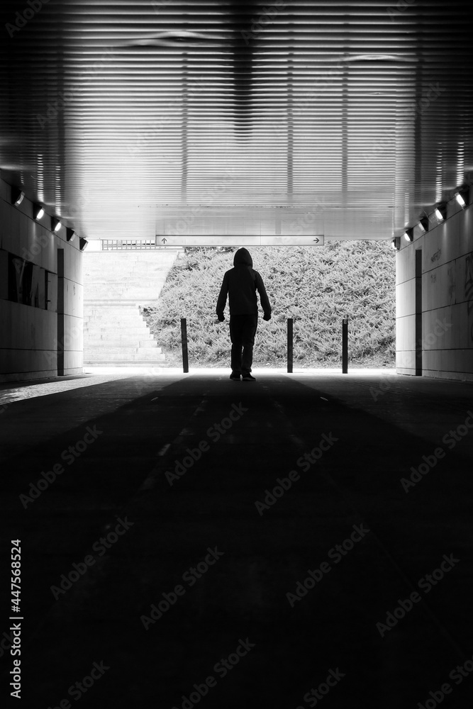Silhouettes in the tunnel - man walking through empty, dark corridor. Underground passage. Unpleasant, dark place. Stranger, danger, safety concept. Black and white
