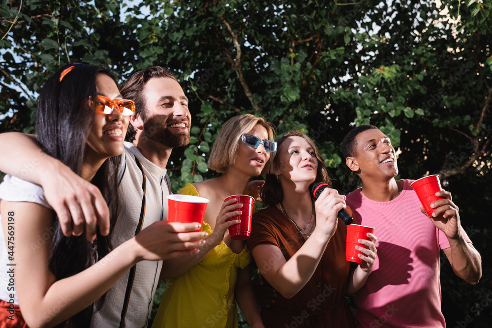joyful multiethnic friends hugging and singing karaoke during summer party joyful multiethnic friends hugging and singing karaoke during summer party
