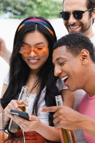 excited multiethnic friends looking at mobile phone during beer party