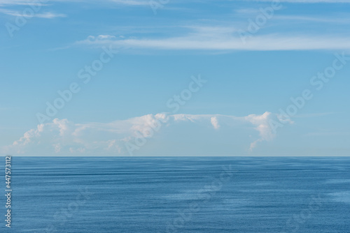 Blue, little cloudy sky over the calm Pacific Ocean.