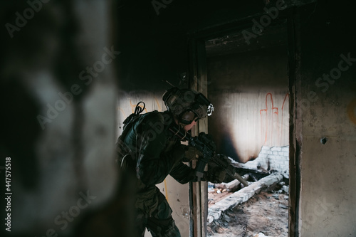 Military man with assault rifle standing inside building, he is ready for combat © romankosolapov