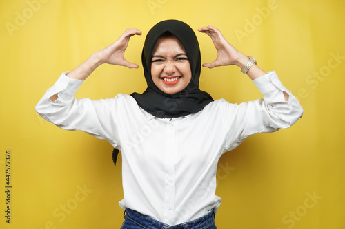 Beautiful young asian muslim woman shocked, dizzy, stressed, unhappy, many problems, want solution, with hands on head isolated on yellow background © MunirSr