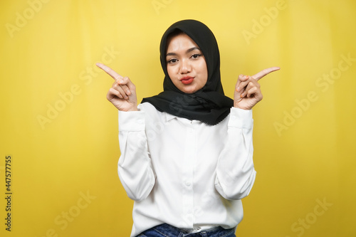 Beautiful asian young muslim woman with mouth watering, hand pointing at empty space presenting something, isolated on yellow background