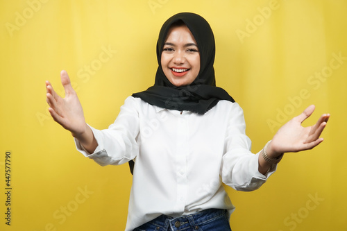 Beautiful young asian muslim woman smiling cheerfully, with open arms to camera, welcome sign hand, hand sign wanting to hug, isolated on yellow background