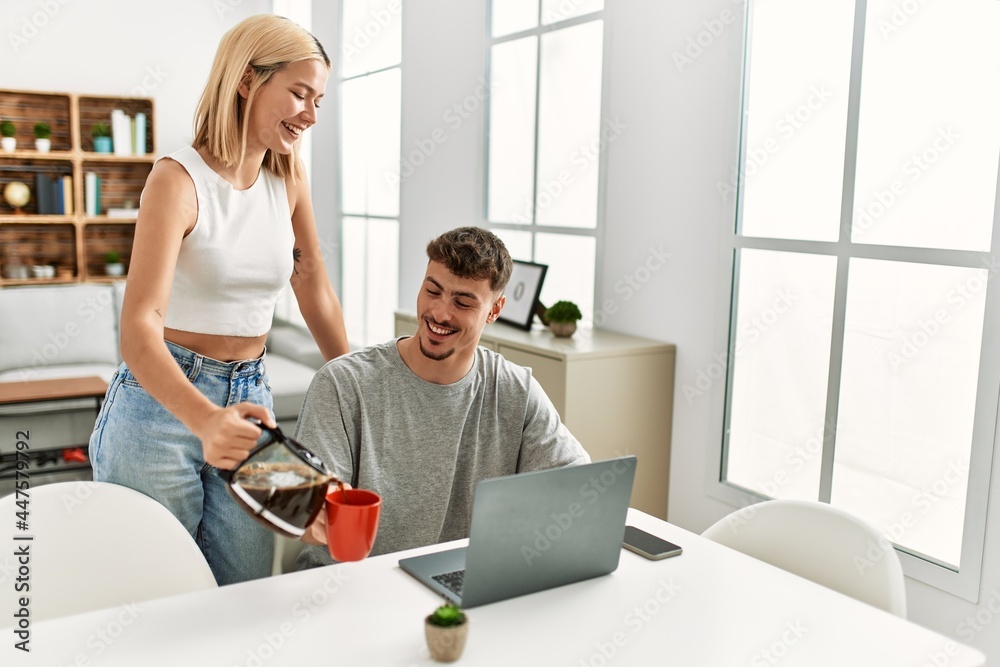 Man working using laptop at home and his girlfriend pouring coffee. Man working using laptop at home and his girlfriend pouring coffee.