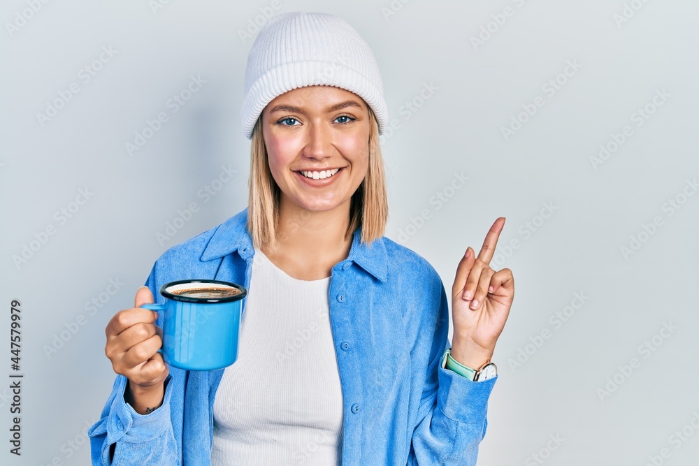 Beautiful blonde woman drinking a cup of coffee smiling happy pointing with hand and finger to the side Beautiful blonde woman drinking a cup of coffee smiling happy pointing with hand and finger to the side