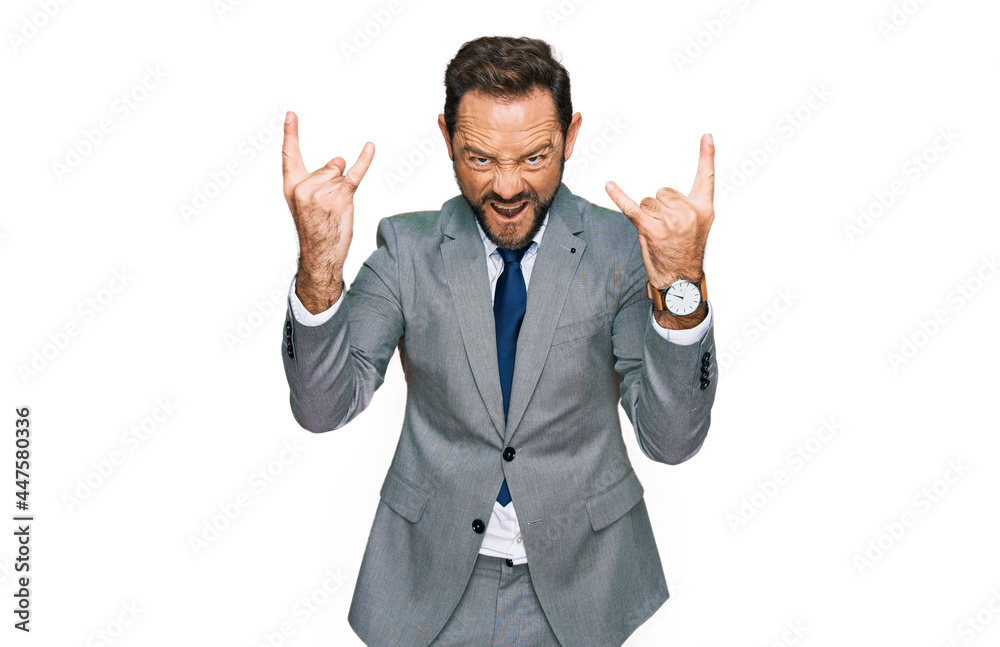 Middle age man wearing business clothes shouting with crazy expression doing rock symbol with hands up. music star. heavy music concept.