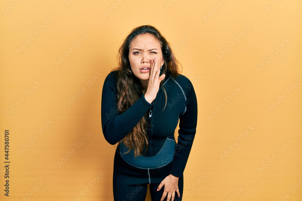 Young hispanic girl wearing diver neoprene uniform hand on mouth telling secret rumor, whispering malicious talk conversation Young hispanic girl wearing diver neoprene uniform hand on mouth telling secret rumor, whispering malicious talk conversation