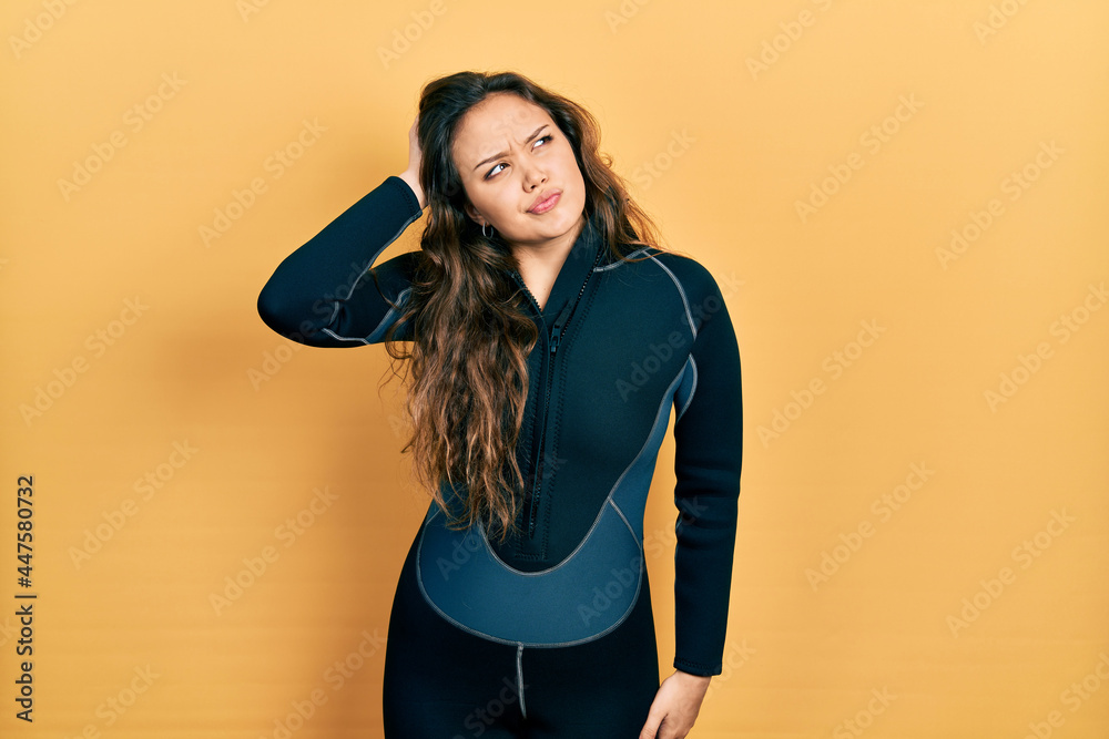 Young hispanic girl wearing diver neoprene uniform confuse and wondering about question. uncertain with doubt, thinking with hand on head. pensive concept. Young hispanic girl wearing diver neoprene uniform confuse and wondering about question. uncertain with doubt, thinking with hand on head. pensive concept.