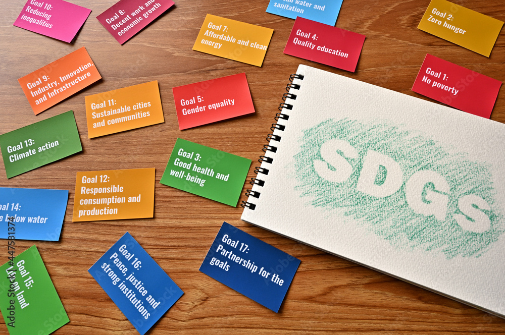 There is a card with the 17 goals of the SDGs on the desk. Beside it, there is a sketchbook with the letters of the SDGs. There is a card with the 17 goals of the SDGs on the desk. Beside it, there is a sketchbook with the letters of the SDGs.
