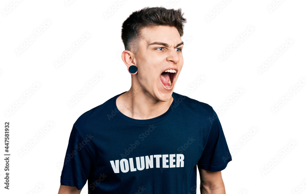 Young caucasian boy with ears dilation wearing volunteer t shirt angry and mad screaming frustrated and furious, shouting with anger. rage and aggressive concept.