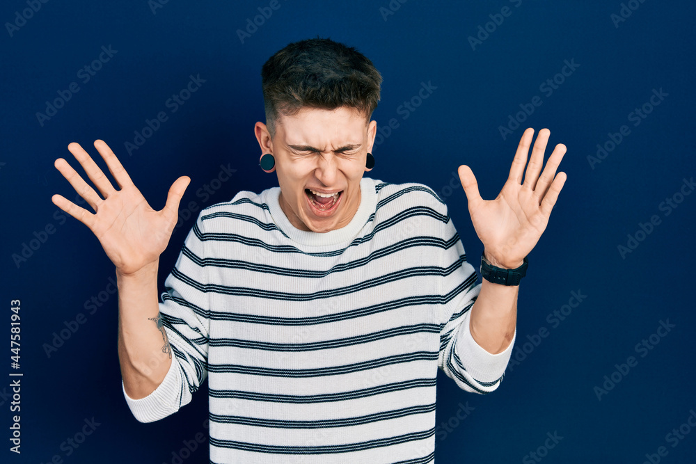 Young caucasian boy with ears dilation wearing casual striped shirt celebrating mad and crazy for success with arms raised and closed eyes screaming excited. winner concept